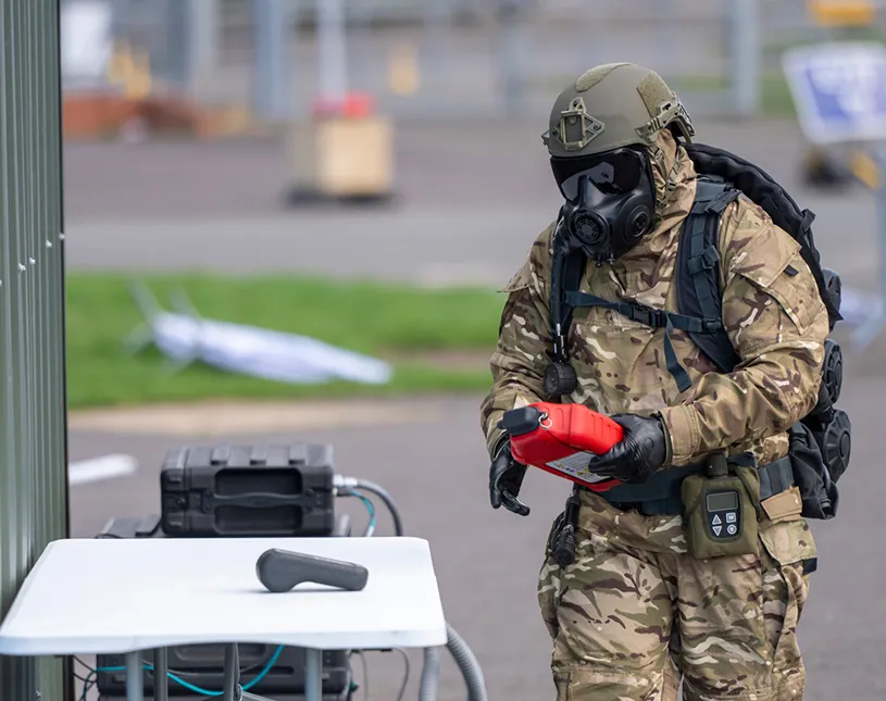 A participant in protective equipment handles a device during an outdoor demonstration.