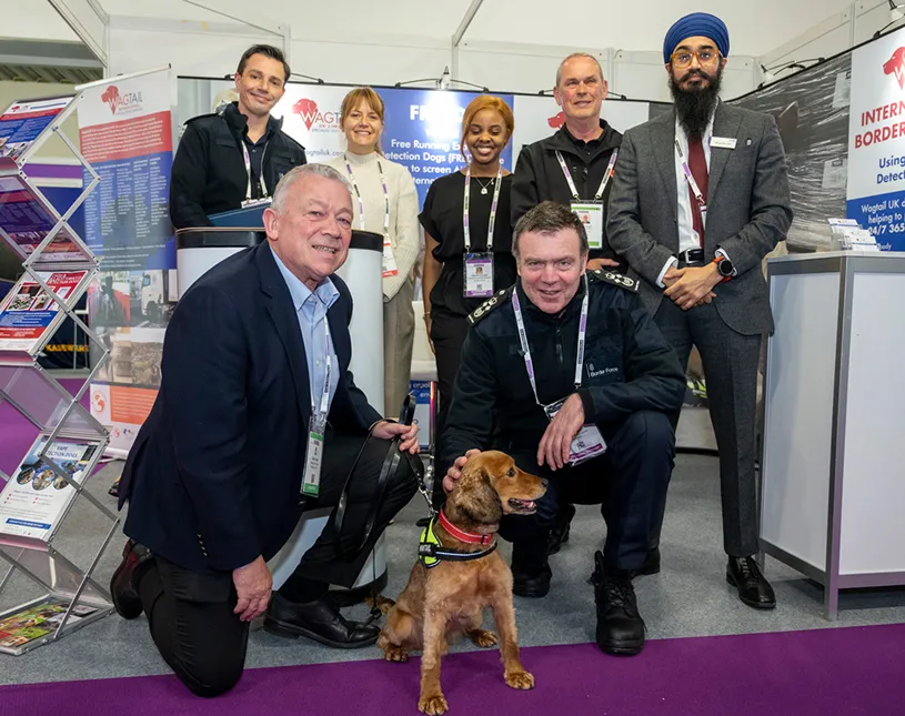 Visitors and exhibitors gather beside a dog on an exhibition stand at Security & Policing.