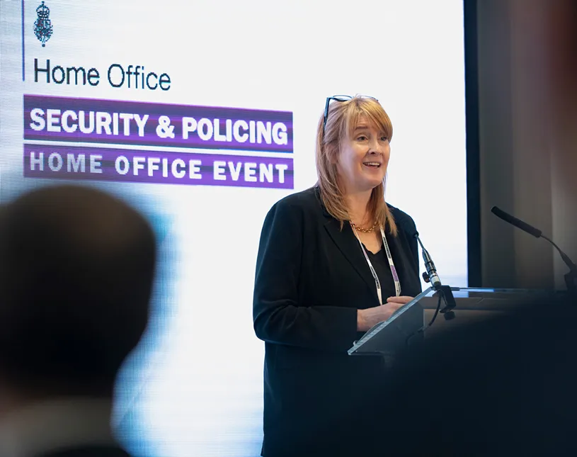A speaker presents at a lectern in front of Security & Policing branding.