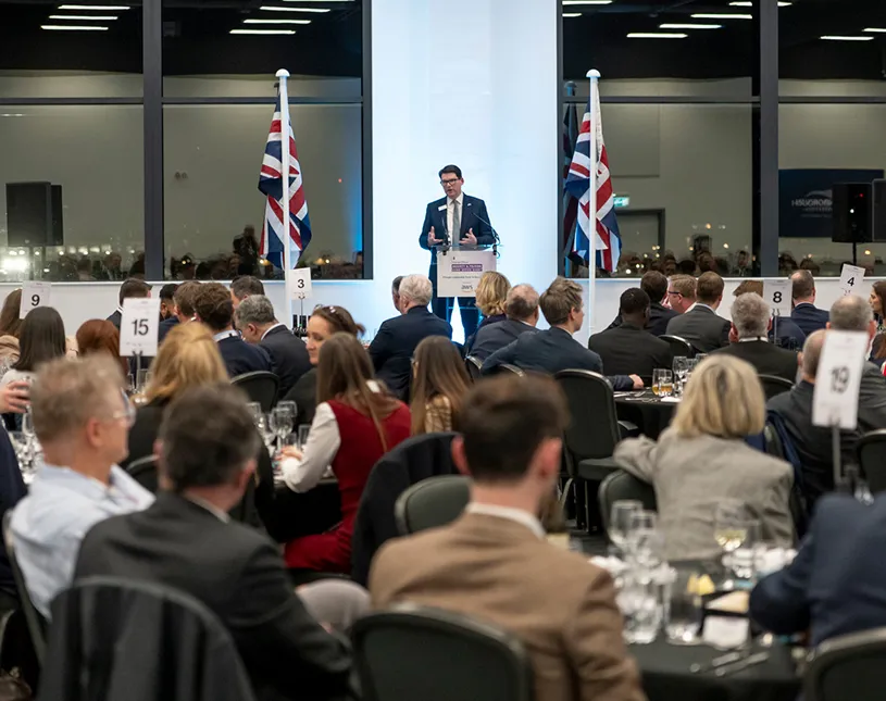 A speaker addresses guests seated at tables during a Security & Policing dinner.