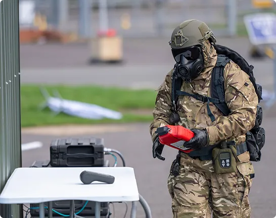 A participant in protective equipment handles a device during an outdoor demonstration.