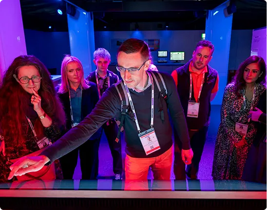 Visitors gather around an illuminated interactive table in the Immersive Experience.